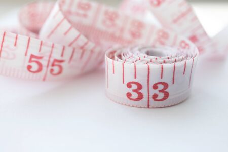 Close-up cloth tape measure with red numbers rolled up on white background. Body measure with centimeters and inchesの写真素材
