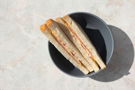Two sanwiches with ham, cheese and tomatoes in gray deep plate on light  marbled table. Homemade...