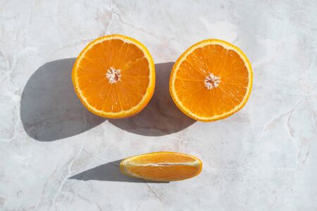 Top view on halved orange and slice on light background. Smiling face, playfull summer mood.の写真素材