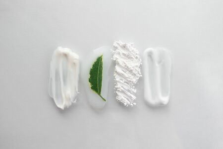 Set of smear beauty cosmetic product and fresh green leaf. Moisturizer, translucent loose powder, soap, facial mask and cleanser isolated on white background. Natural skin care conceptの写真素材