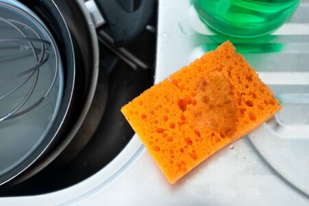 Orange sponge with detergent in kitchen sink, close-up. Needing washing-up. Cleaning chores. Service cleaning up conceptの写真素材