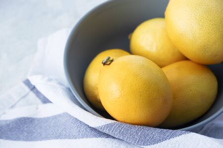 Close-up yellow lemon in bowl and towel on marble table. Raw fresh organic ripe citrus fruits with...