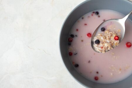 Close-up spoon with oat, berry and milk in gray bowl at breakfast on marble table background with copy space. Aboveの写真素材
