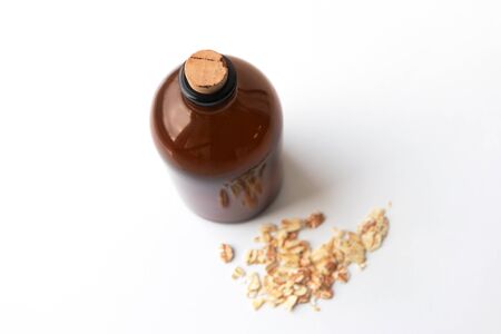 Natural ubtan powder with oatmeal in brown glass bottle for gentle face cleansing on white background, top view. Organic skin care product, body cleanser and scrubの写真素材