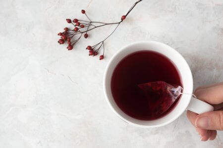 Woman hold white cup with fruity tea in tea pyramid bag. Mug and  red berries on marble background. Cozy winter mood, top viewの写真素材