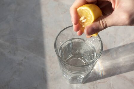 Hand squeezes lemon juice in glass with soda water on marble table background. Detox healthy drink conceptの写真素材