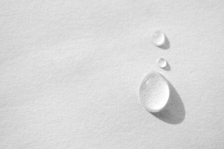 Water drop on white paper textured background with copy space and selective focus, close-up. Concept moisturizing macro, top viewの写真素材