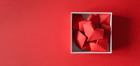 Origami heart in white gift box on red background, top view. Valentine's day surprise with copy space horizontal banner format.の写真素材