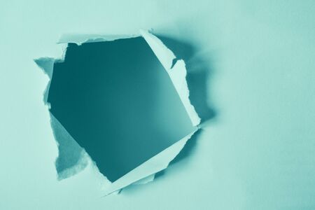 Round damaged hole in paper mint color with copy space. Torn ripped paper sheet with selective...