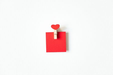 Red heart wooden mini clothespin and paper blank note on white background, above. Cute Valentine's day card or wedding party inviteの写真素材