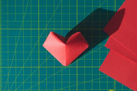 Heart origami and red paper sheets on green cutting mat. Making hand made Valentine's Day elements,...