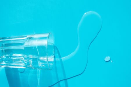 Glass and spilled water on blue background. Concept water balance in organism, healthcare