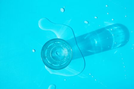Empty glass and splash drops water on blue background. Concept water balance in organism, healthcareの写真素材
