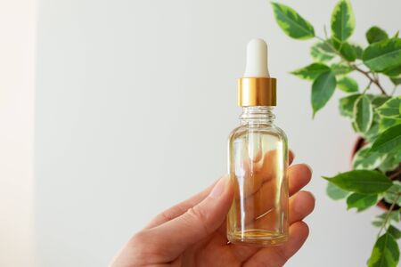 Woman hand holding serum essence in glass bottle and leaves on white background. Skin care beauty product. Face moisturizer. Concept natural and organic cosmetic, copy spaceの写真素材