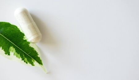 Close-up medical pill capsule and plant leaf on white background with copy space, above. Concept alternative medicine, horizontal banner fornatの写真素材