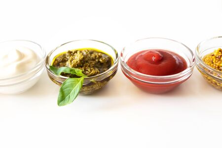 Close-up various sauce and dip with selective focus on white background. Mayonnaise, pesto, ketchup and french mustard in glass bowlsの写真素材