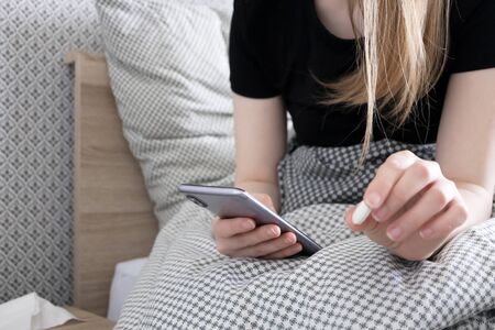 Woman use smartphone and take pill at bed, selective focus. Girl feeling sick at home, indoors....