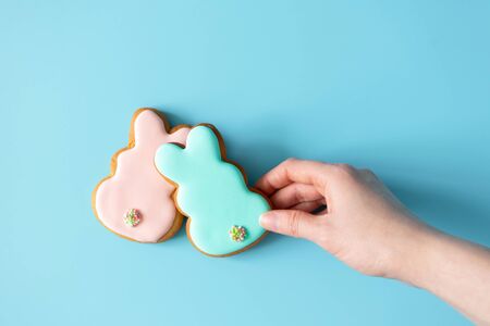 Woman takink Easter cookies rabbit shape on blue background with copy space, top view