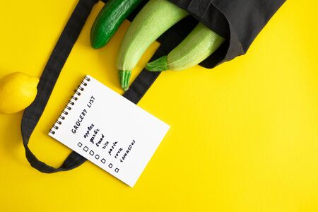 Grocery list in paper notepad and cotton eco black bag with zucchini and cucumber, lemon on yellow background with copy space, above. Concept dietary and healthy lifestyle, horizontalの写真素材