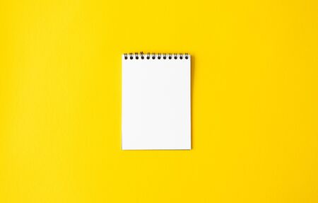 Empty white paper spiral notepad on yellow background. Mockup memo or diary, top view. Minimalistic...