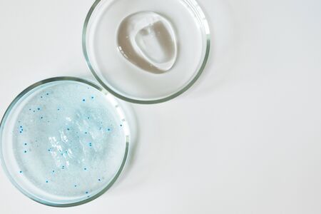 Blue shower gel with scrub grain with bubbles and transparent shampoo smudge in glass petri dish on...