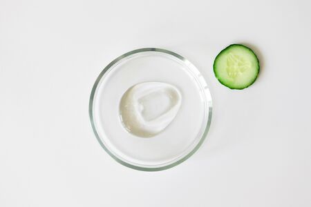 Slice of cucumber and transparent cosmetic gel smudge in glass petri dish on white background. Making natural organic cosmetics. Purity facial cleanser, peeling, shampoo or shower gelの写真素材
