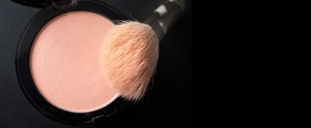 Makeup brush and peach blush with selective focus on black background horizontal banner format with...