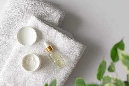 Oil serum essence dropper and moisturizer cream on towels on white background with copy space. Beauty products for facial skin care and defocused leaves, aboveの写真素材