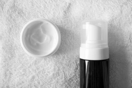 Close-up moisturizer cream and cleanser foam in brown container with dispenser on white bathroom towel background. Daily routine facial skincare, top viewの写真素材