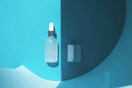 Glass bottle essential collagen anti-aging serum and eye moisturizer cream on blue paper background, top view. Skincare beauty productの写真素材