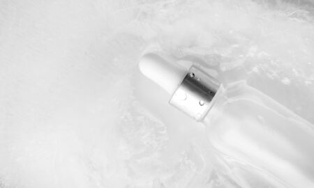 Close-up serum in glass bottle with water drops in ice background and selective focus, horizontal banner format. Concept summertime beauty product with copy space, top view. Cooling summer facial careの写真素材