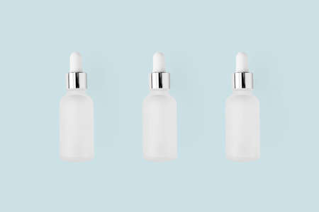 Vitamin E serum moisturizer in glass bottles with dropper on light blue minimalist pastel...