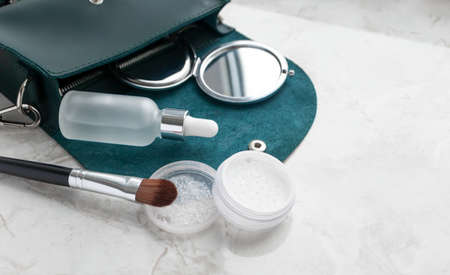 Close-up cute tiny emerald female bag with cosmetic product on marble table. Transparent powder,...