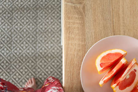 Grapefruit slices on pink plate on wooden table with selective focus and woman on background, top view. Fresh citrus fruit for healthy eating. Lifestyle food photoの写真素材