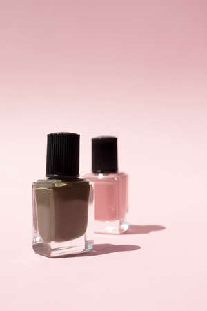 Two colorful nail polish in glass bottle on pink background with copy space, vertical. Beauty product for manicure and nail care in minimalist style for brandingの写真素材