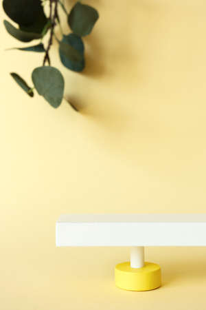 Abstract pedestal on pastel yellow background with copy space and defocused eucalyptus leaves, front view. Minimalist scene with podium for promotion, cosmetic product show, verticalの写真素材