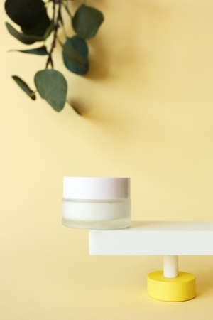 Mockup moisturizer cream in jar standing on abstract pedestal on pastel yellow background with copy...