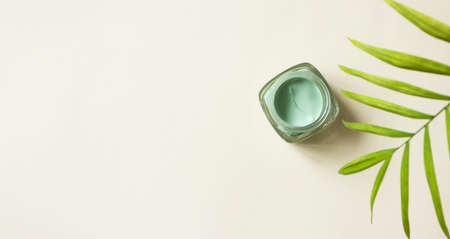 Facial green clay mask and defocused tropical leaf on light beige background with copy space, above. Skin care beauty detox product horizontal format bannerの写真素材