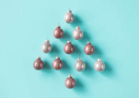 Pink Christmas balls toys lay in fir tree shape minimalist composition on blue background, top view....