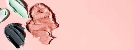 Various facial clay cosmetic masks smudge on pink background with copy space horizontal banner format. Cosmetic texture black, pink and green claysの写真素材