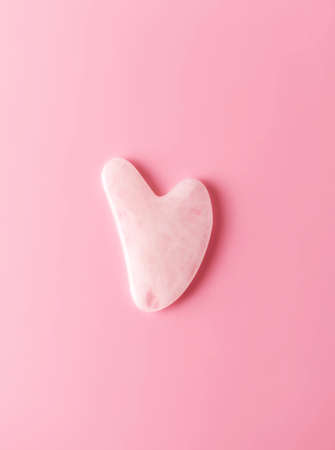 Gua sha on pink background with copy space, top view. Trendy skincare facial massager tool guasha,...