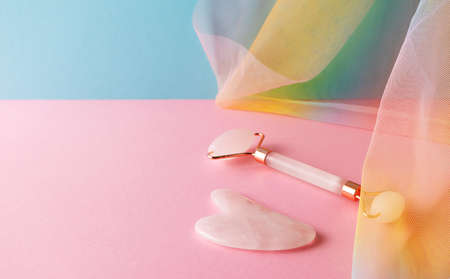 Gua sha and quartz facial roller for skincare massage on blue pink background with colorful rainbow...