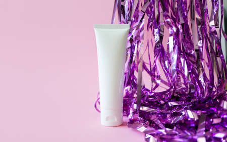 White plastic tube mockup with moisturizer cream, shampoo or facial cleanser and holiday tinsel on pink backgroundの写真素材