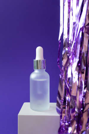 Serum mockup with pipette and holiday tinsel on cube podium on violet background, verticalの写真素材
