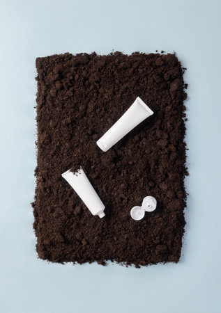 Plastic cosmetic tubes on soil ground on blue background flat lay composition, top view. Concept recycling of cosmetic waste from the beauty industryの写真素材
