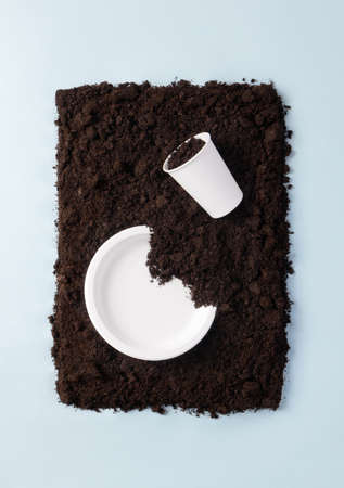 Paper plate and glass on soil on blue flat lay composition, top view. Compostable or biodegradable dinnerware concept, verticalの写真素材