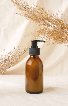 Bottle with pump for beauty product mockup on linen drapery and dry branch of meadow plant. Concept eco organic cosmetic with natural extracts. Mockup skincare cosmetic productの写真素材