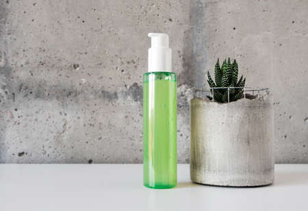 Natural green facial cleanser with bubbles and a succulent in concrete pot on white desk on cement wall backgroundの写真素材