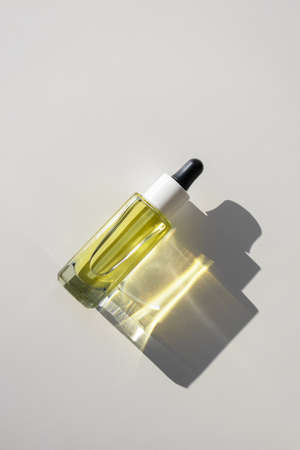 Facial yellow oil serum glass bottle with pipette on white background with bright sunbeam reflection, top viewの写真素材