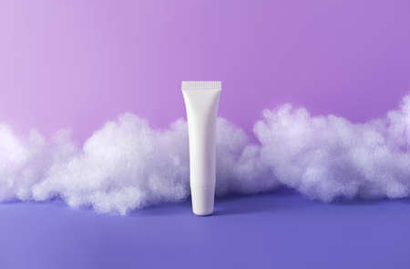 Lip balm with fluffy clouds on violet background. Concept care with sensitive skin. Creative still-life photo, vertical. Template mockups beauty productの写真素材